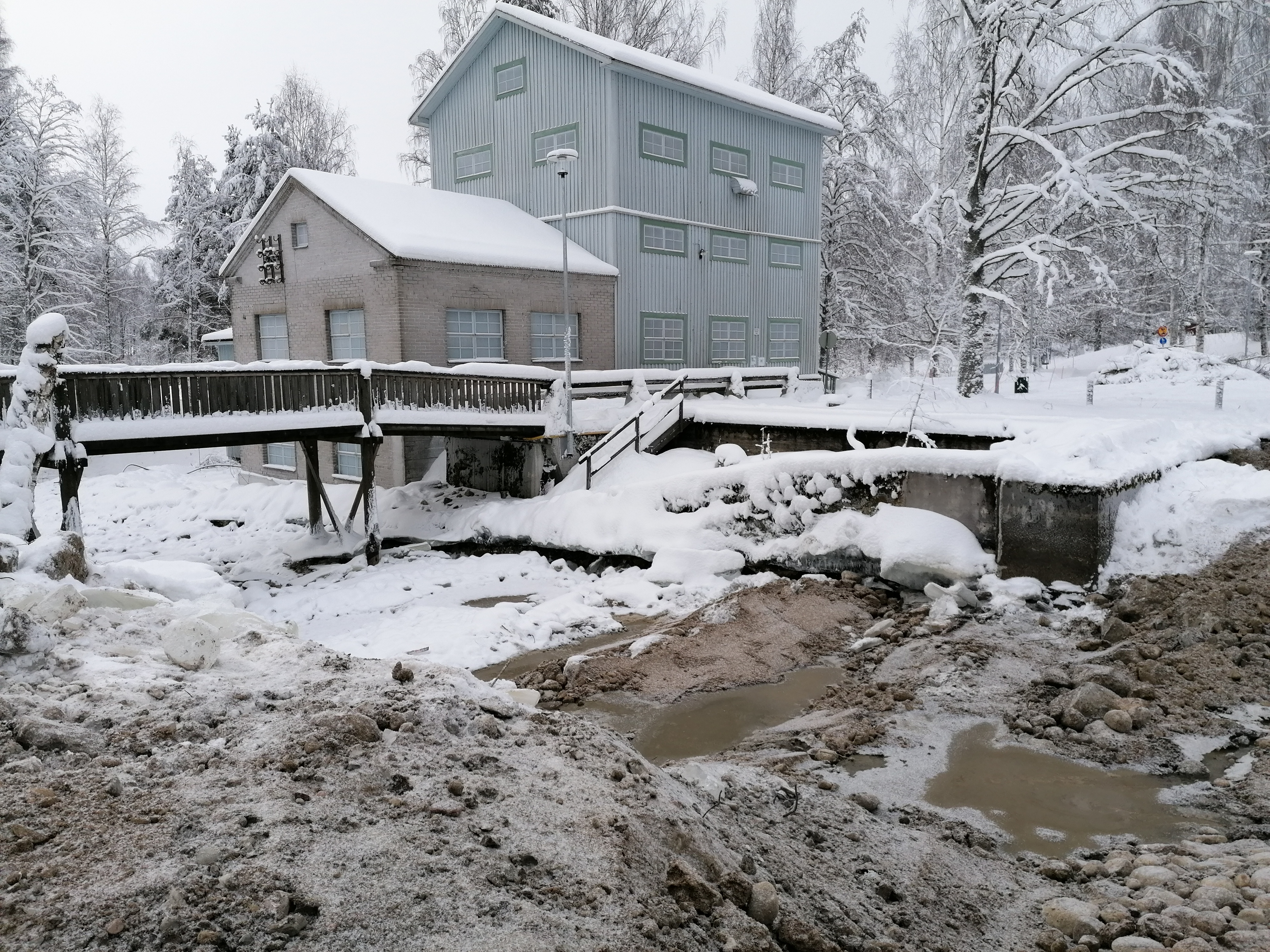 Talvinen kuva koskityömaasta, jossa on vanha puinen mylly ja purettu myllypato.