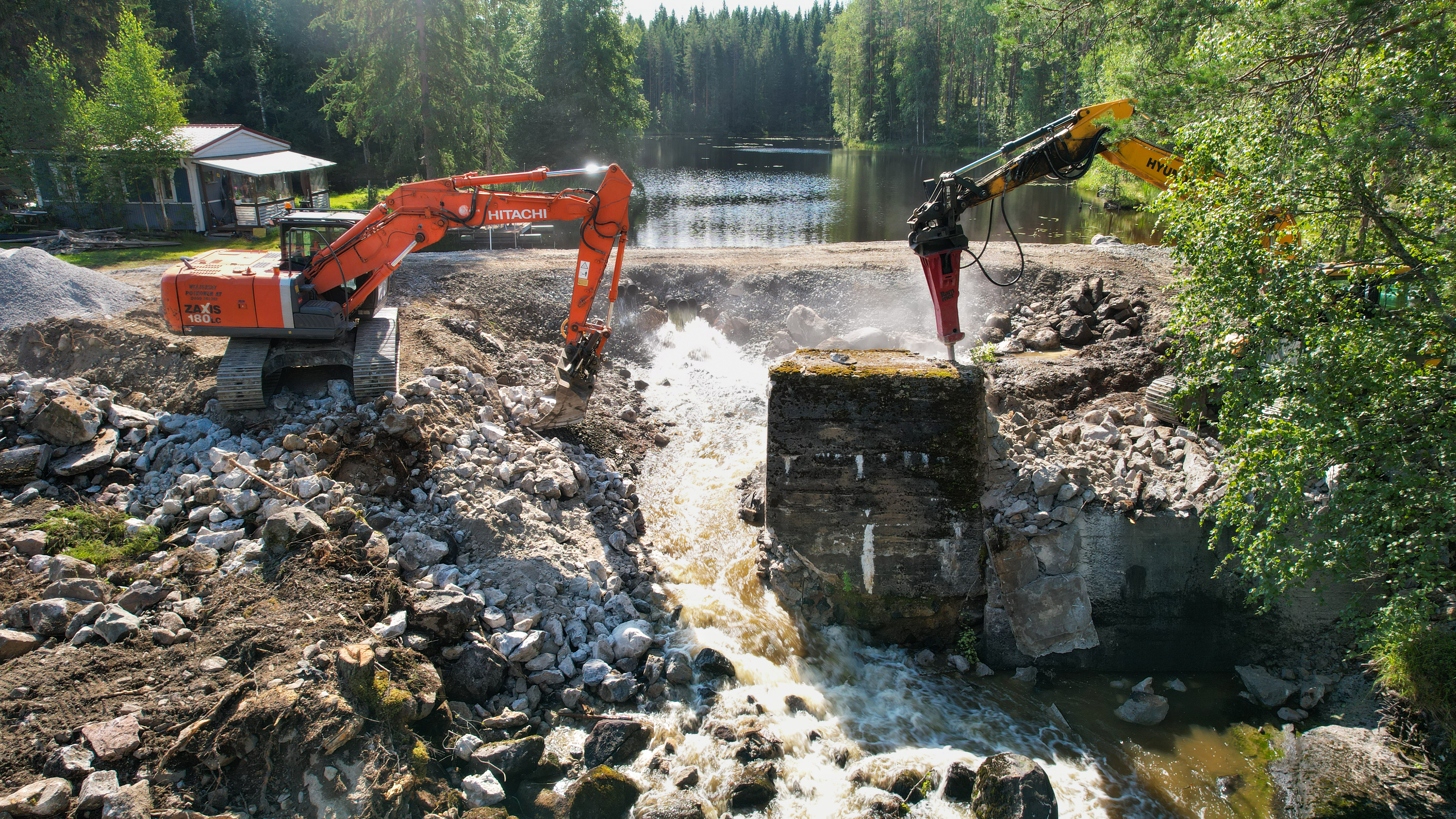 Kaivinkoneet purkavat patoa Rutajoen Seinäkoskella.
